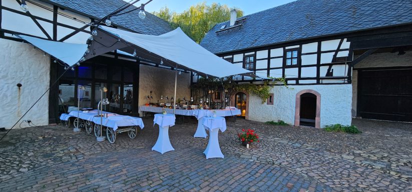Rustikaler Gastronomiebereich mit gedeckten Tischen und Sonnenschutz im Freien.