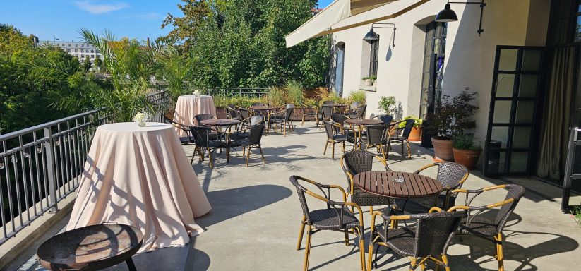 Gepflegte Terrasse mit Tischen und Stühlen, umgeben von grüner Vegetation.