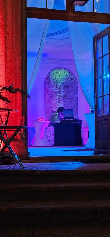 Bunte Beleuchtung in einem Raum mit Tischen und Dekorationen, im Hintergrund eine Person.