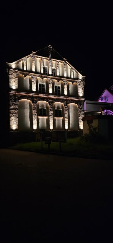 Historisches Gebäude mit beleuchteter Fassade, nachts sichtbar.
