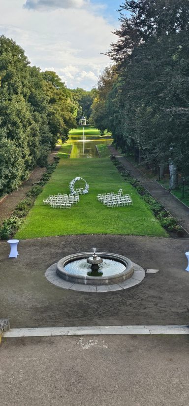 Blick auf einen gepflegten Garten mit Rasen, Wasserbecken und angeordneten Blumenbeeten.