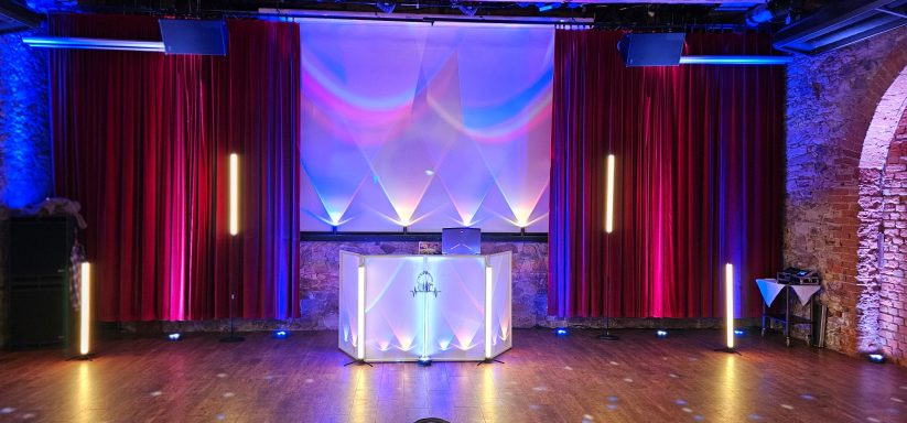 Eventlocation mit rotem Vorhang, bunten Ambientebeleuchtung und modernem DJ Pult