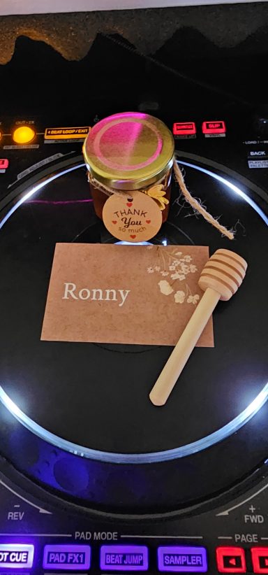Ein Glas Honig mit einem Holzlöffel und einer Karte mit dem Namen DJ Ronny LE.
