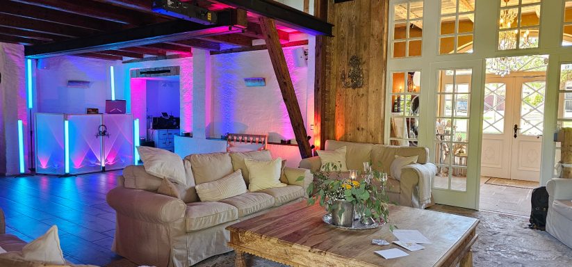 Gemütlicher Wohnraum mit bunten Lichtern, Couch und großen Fenstern.